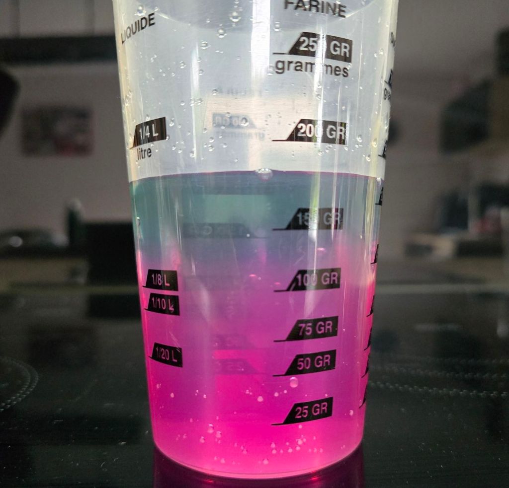 Infusion de violette dans un verre doseur, bleu-vert en haut et rose vif après ajout de citron en bas